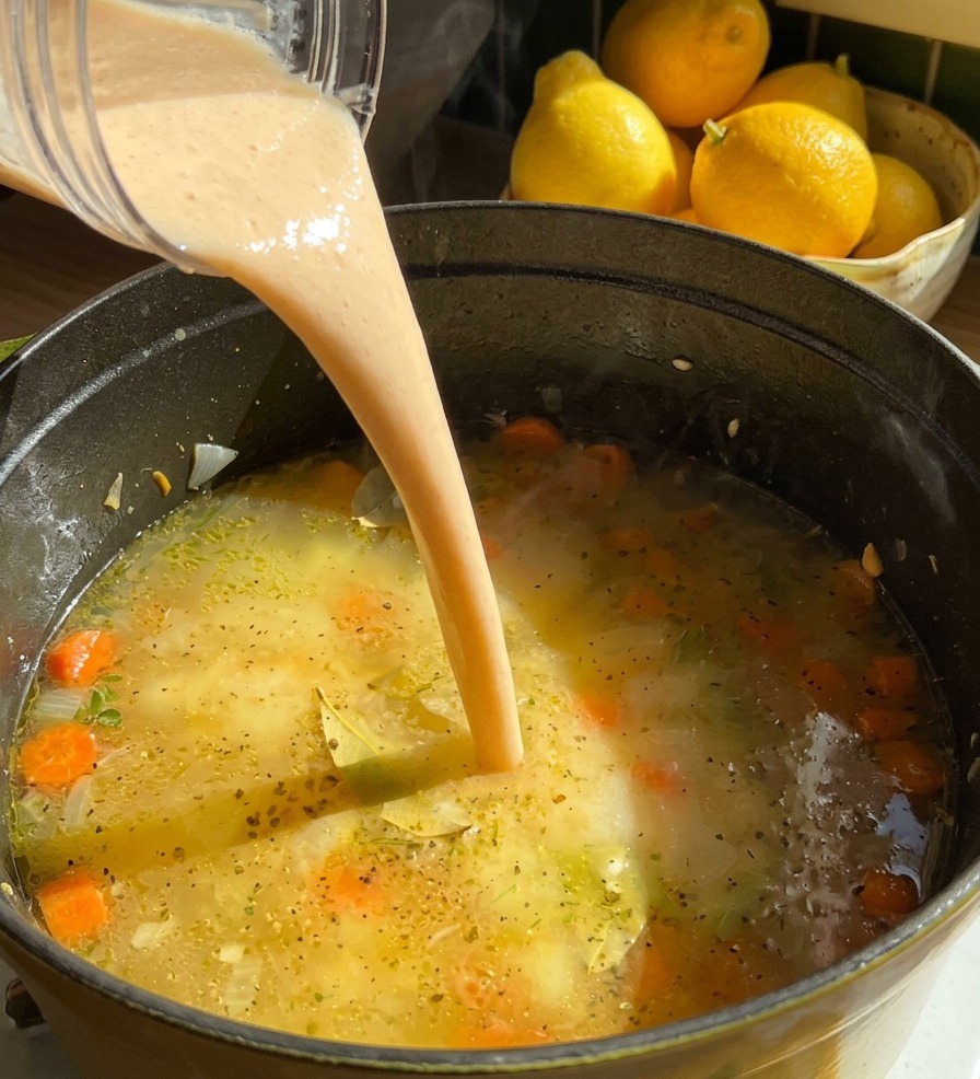 Ein Strahl dickflüssiges, cremiges Bohnenpüree wird aus einem Mixerbecher in einen Topf mit köchelnder Suppe und Karottenscheiben gegossen.