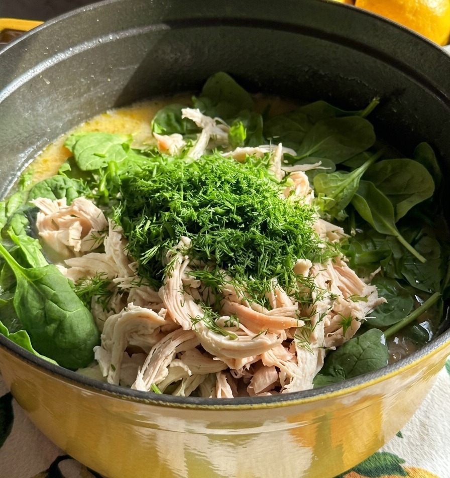 Ein Topf Suppe, garniert mit gezupftem weißen Hühnerfleisch und einem großen Berg fein gehacktem, frischem grünen Dill.