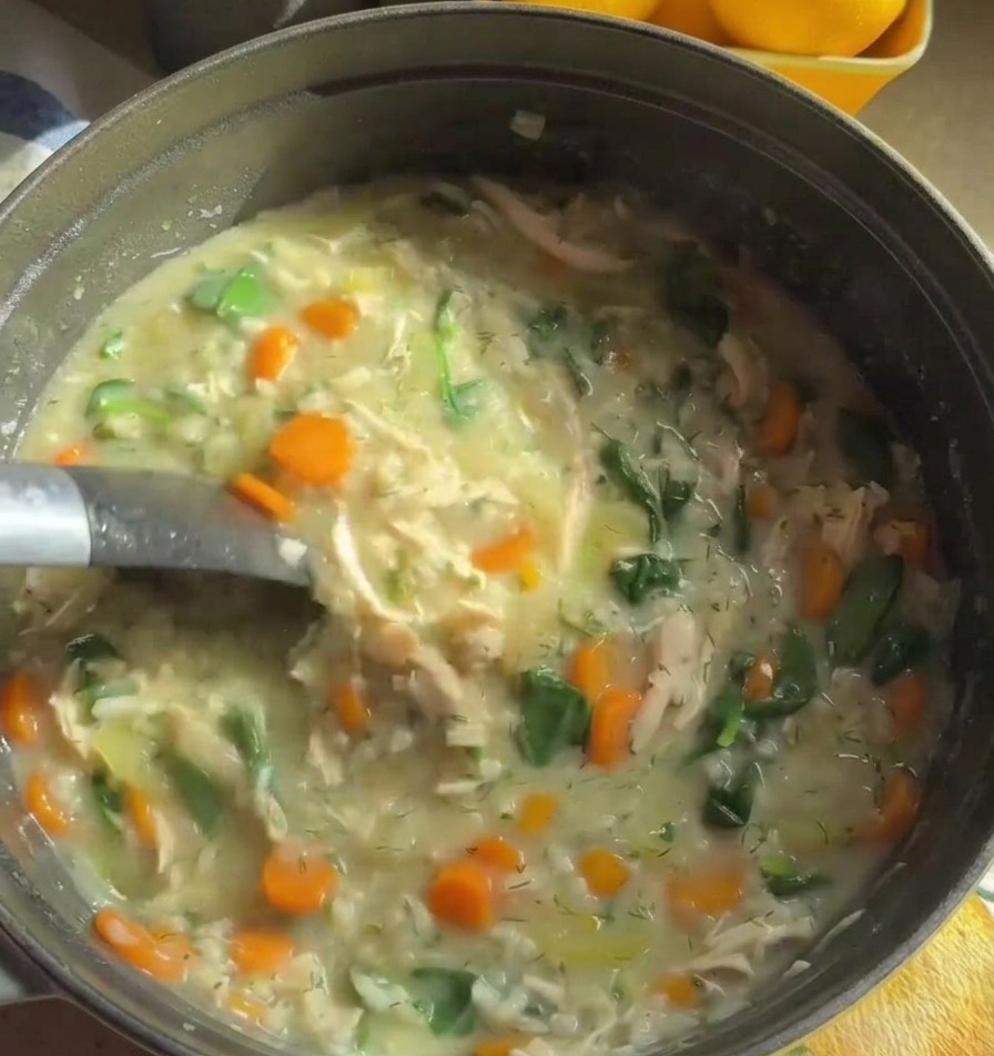 Eine Metallkelle rührt durch eine sämige, cremige Hühnersuppe voller orangefarbener Karotten und grünem Spinat.