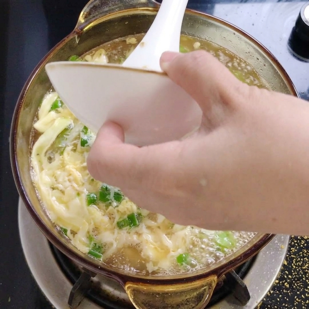Gehackte grüne Kräuter werden aus einer kleinen weißen Schüssel in die dampfende Okrasuppe gegeben.