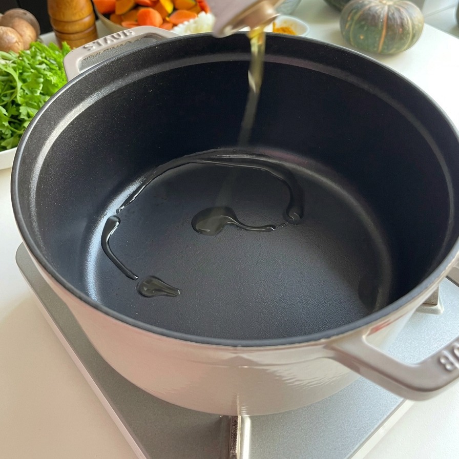 Klares Speiseöl wird aus einer weißen Keramikflasche in einen vorgeheizten, schwarzen Gusseisentopf gegossen.