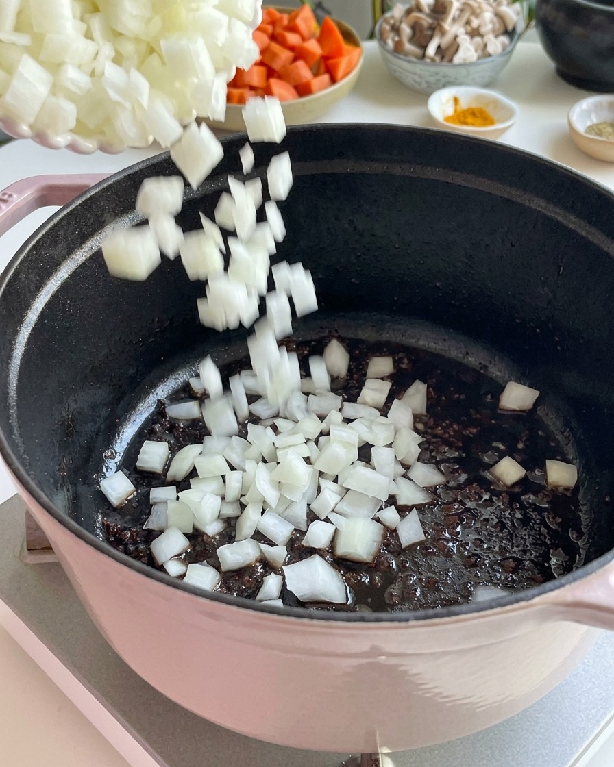 Gewürfelte weiße Zwiebeln werden zum Anschwitzen in einen gusseisernen Topf gegeben.
