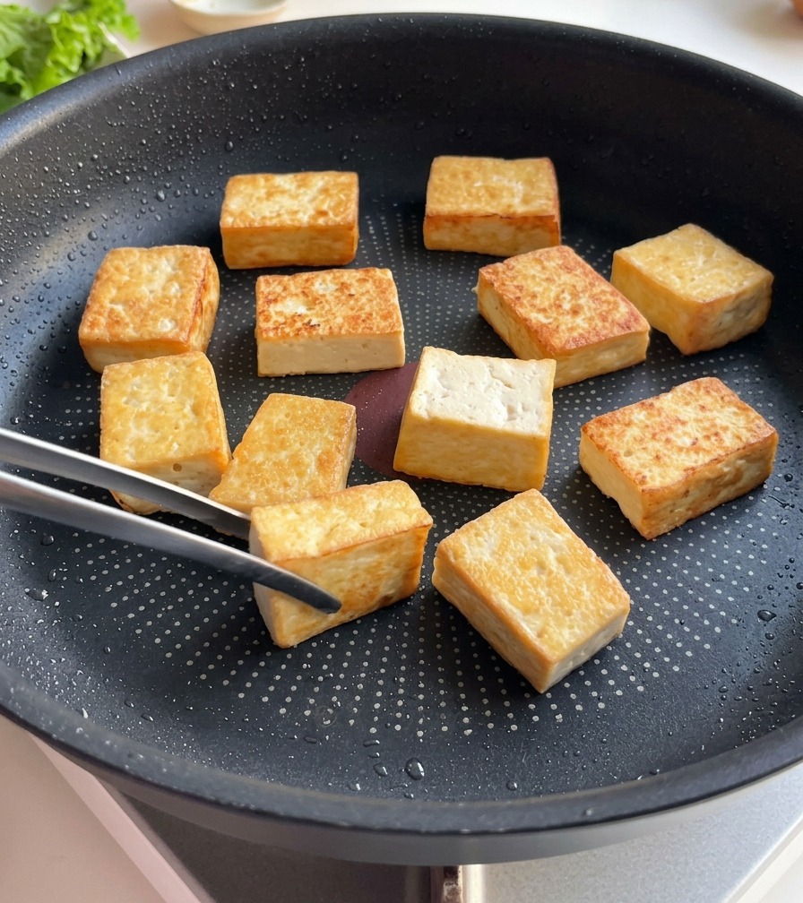 Tofublöcke in einer Bratpfanne zeigen eine tief goldbraune Kruste auf ihren gebratenen Oberflächen.