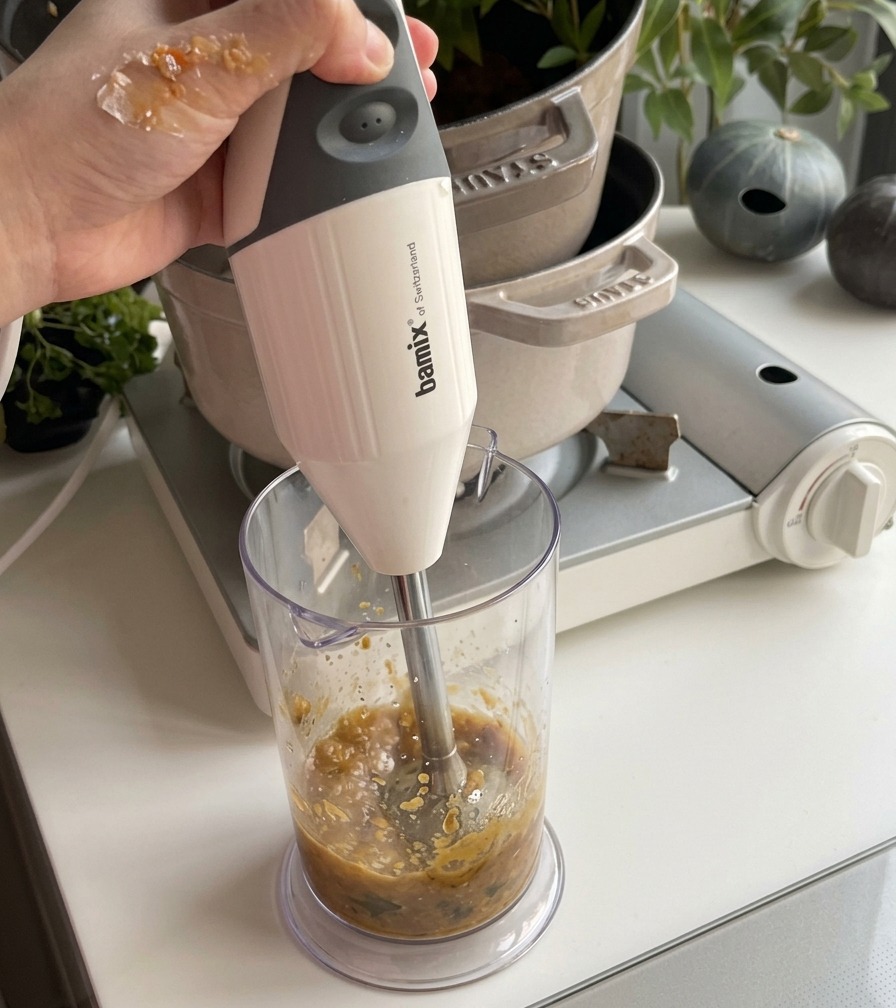 Ein Strahl weißer Kokosmilch wird in einen Topf mit cremiger, orangefarbener Kürbissuppe gegossen und mit einem Pfannenwender verrührt.