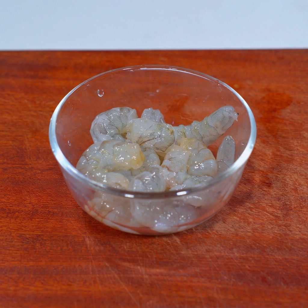 Rohes, geschältes Garnelenfleisch in einer Glasschüssel, bestreut mit Salz und Pilzwürzpulver.