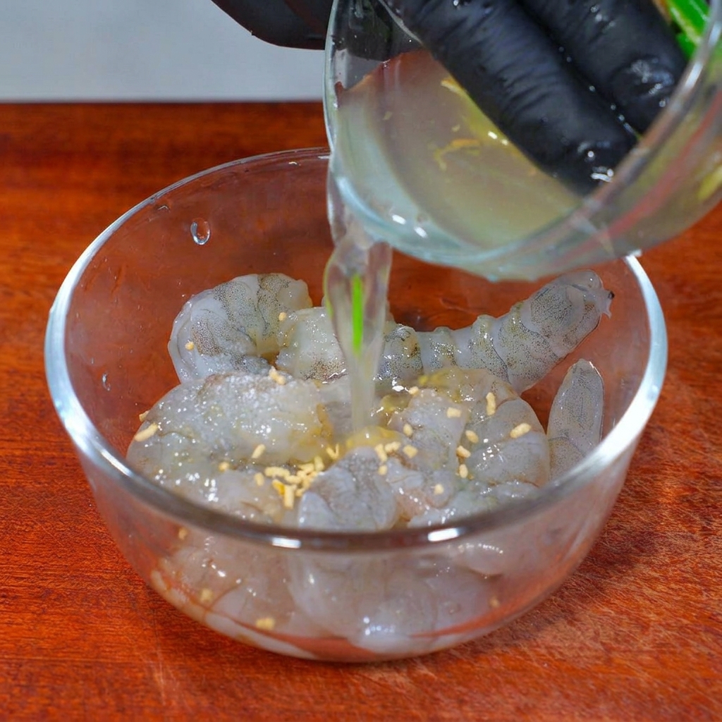 Aromatisches Frühlingszwiebel-Ingwer-Wasser wird in eine Glasschüssel mit gewürzten rohen Garnelen gegossen.