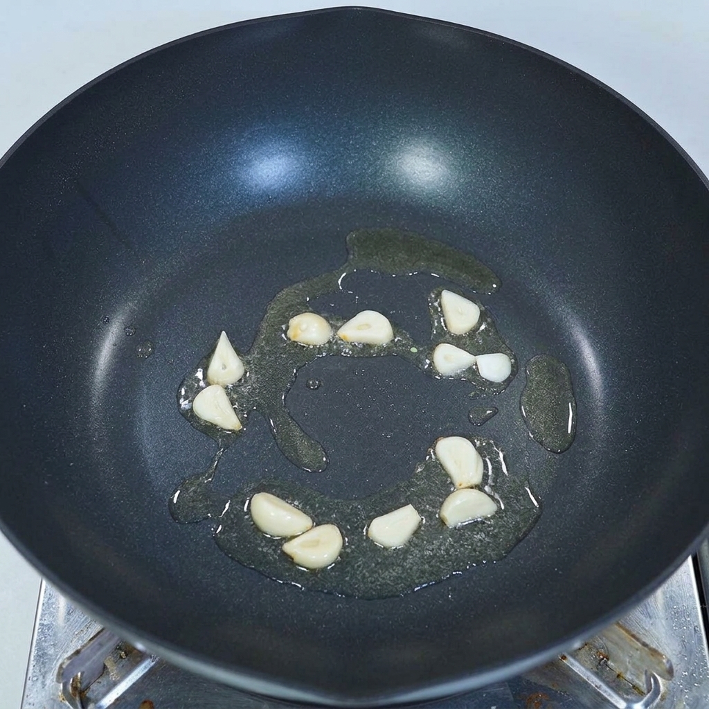 Dünn geschnittene Knoblauchzehen brodeln in etwas Öl am Boden eines dunklen Woks.