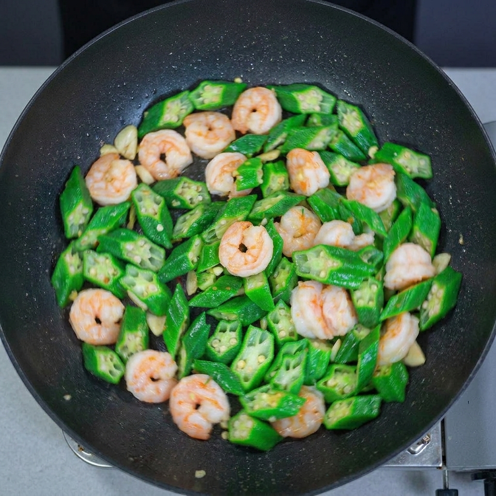 Draufsicht auf einen Wok voller glänzender, pfannengerührter Okraschoten und Garnelen.