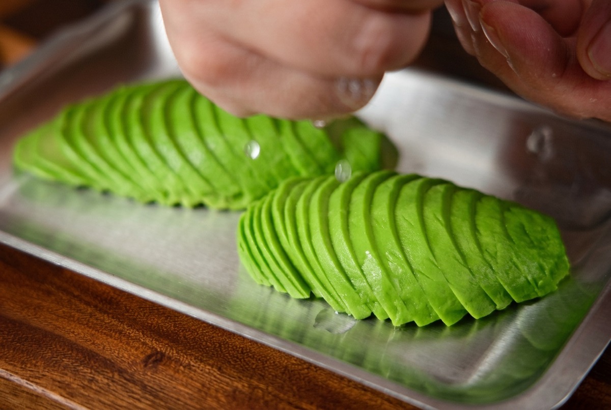 Frischer Zitronensaft wird von Hand über eine Reihe sauber angeordneter Avocadoscheiben gepresst.