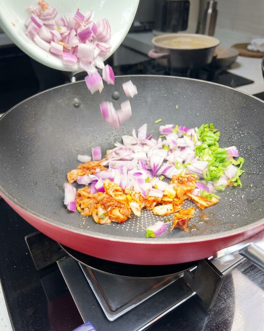 Gehackte rote Zwiebeln, grüner Koriander und orangefarbenes Kimchi werden in einer Bratpfanne geschwenkt.
