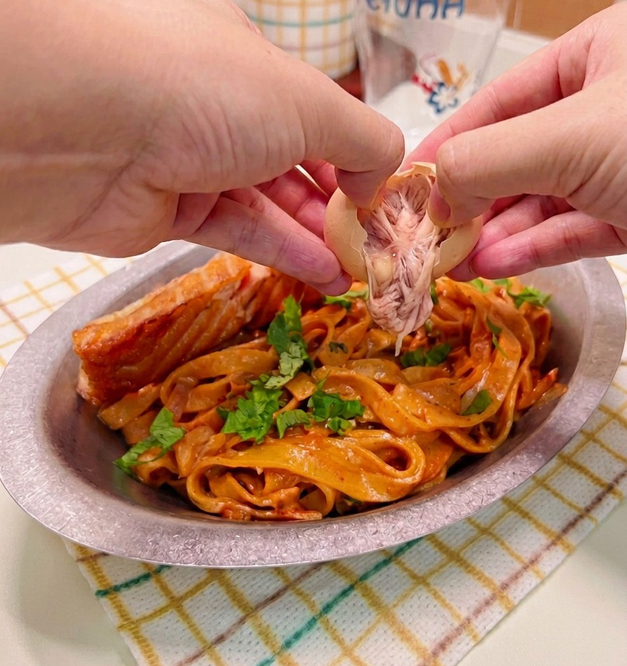 Hände pellen vorsichtig ein weichgekochtes Ei und platzieren es auf einem angerichteten Teller mit scharfer Cremepasta und gebratenem Lachs.
