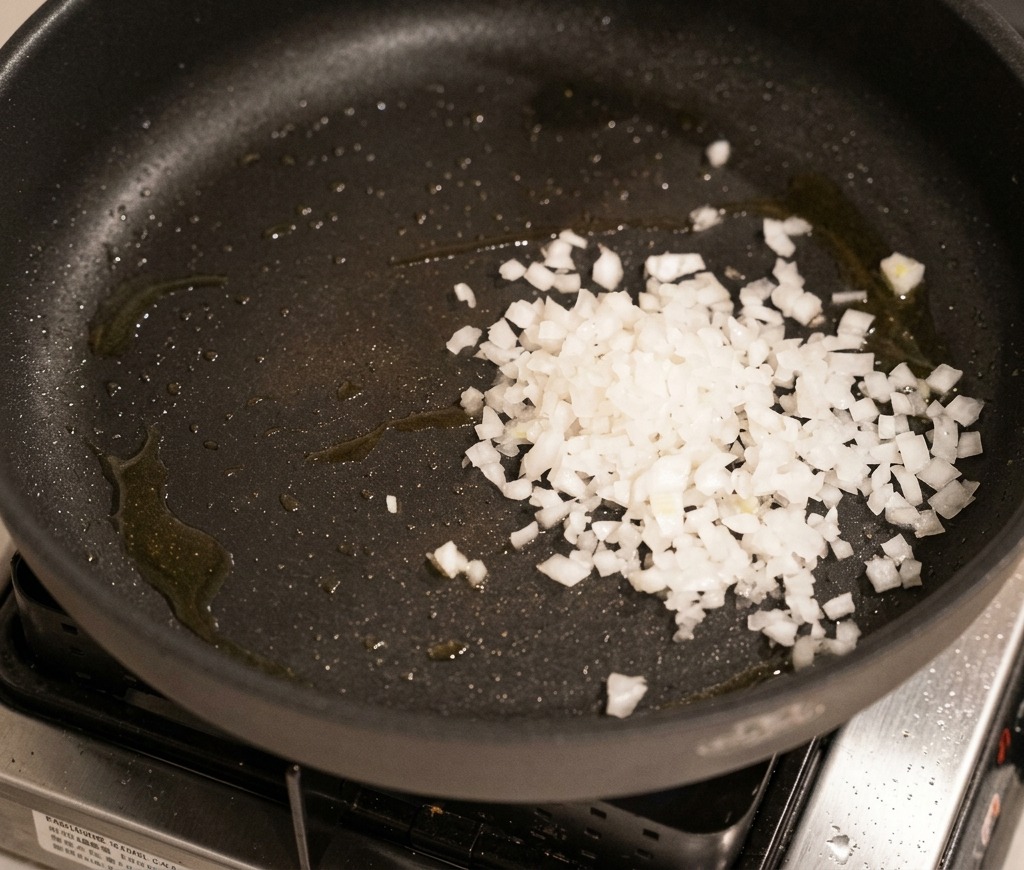 Gewürfelte weiße Zwiebeln werden in einer dunklen Pfanne angedünstet, bis sie glasig und weich sind.