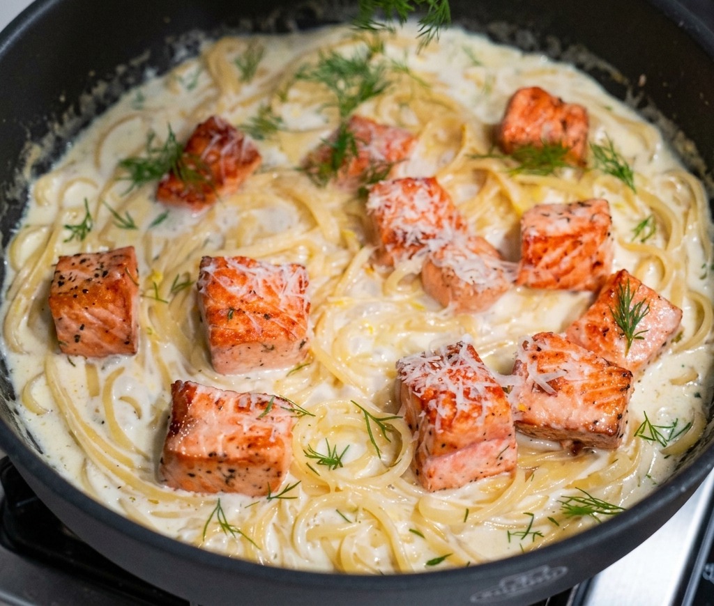 Eine Hand streut gehackten grünen Dill über die fertige Pfanne mit der cremigen Lachs-Pasta.