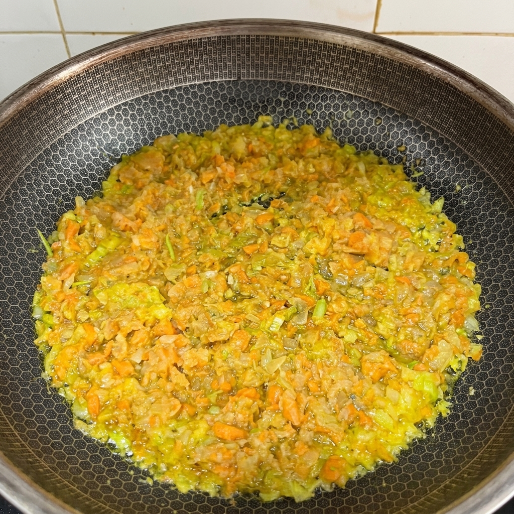Fein gehackte Karotten, Sellerie und Zwiebeln dünsten in einer Pfanne mit geschmolzener Butter.