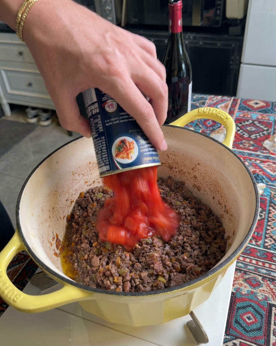 Passierte Tomaten werden in einen Topf mit gebräuntem Fleisch gegossen.