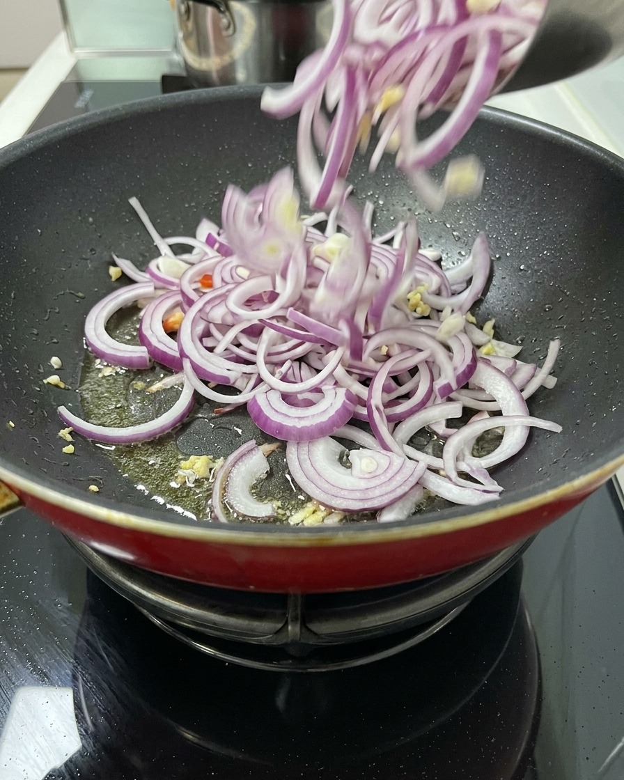 Eine große Menge geschnittener roter Zwiebeln wird aus einer Schüssel in eine Bratpfanne mit Öl und Aromaten gegeben, um sie anzuschwitzen.