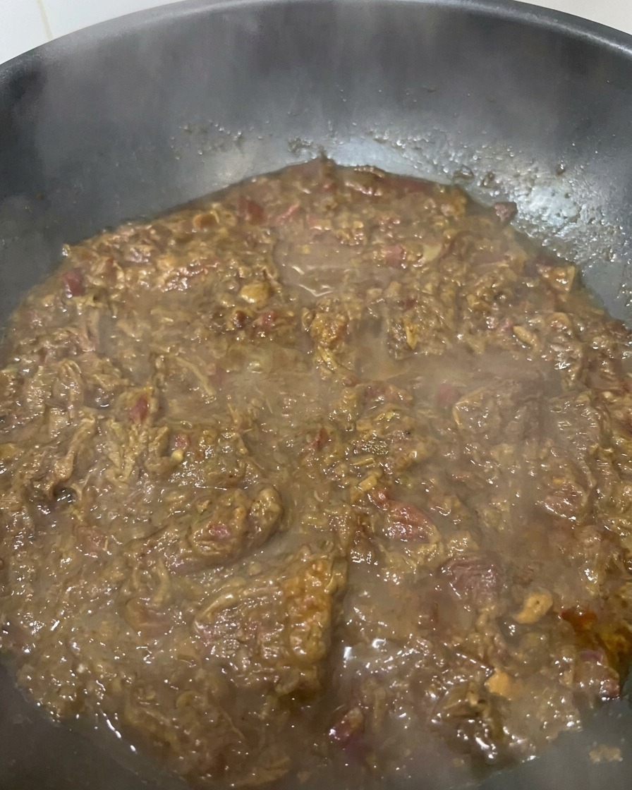 Nahaufnahme einer dicken, dunkelbraunen Zwiebel-Fleisch-Sauce, die in einer pfanne köchelt und eine reichhaltige, marmeladenartige Textur zeigt.