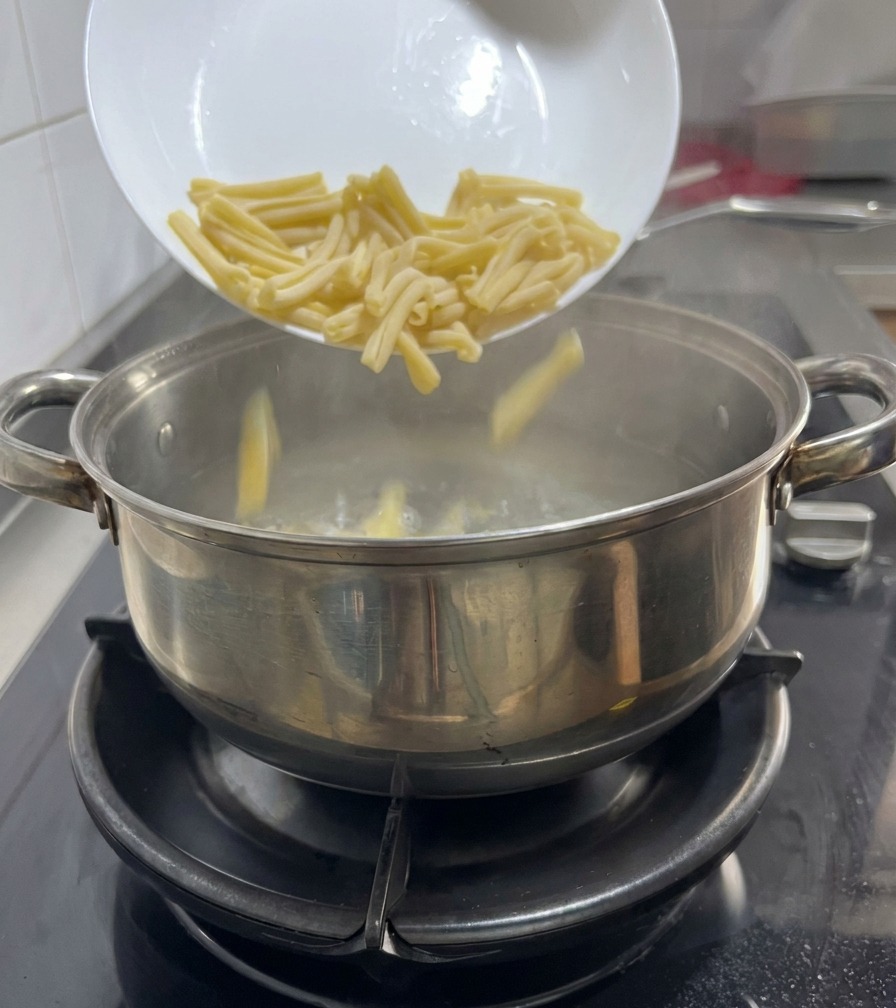 Casarecce-Pasta wird von einem weißen Teller in einen Topf mit kochendem Wasser auf einem Gasherd geschüttet.