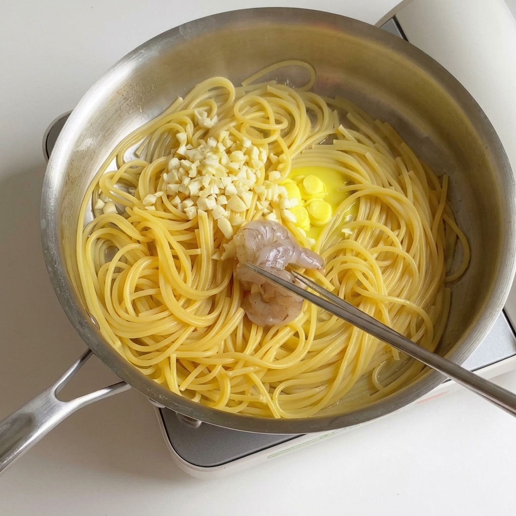 Marinierte Garnelen werden in eine Edelstahlpfanne mit gekochten Spaghetti, schmelzender Butter und gehacktem Knoblauch gegeben.