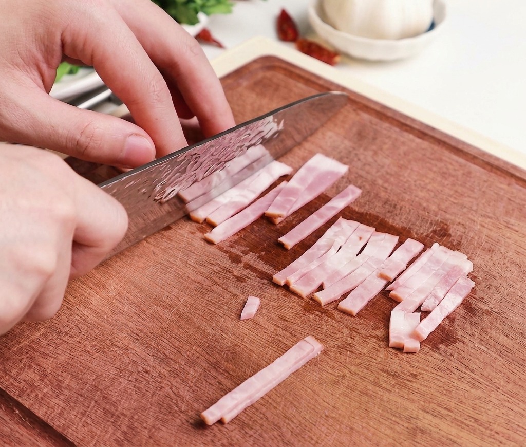 Hände schneiden rohe Speckstreifen mit einem professionellen Kochmesser auf einem Holzschneidebrett in kleine, gleichmäßige Stücke.