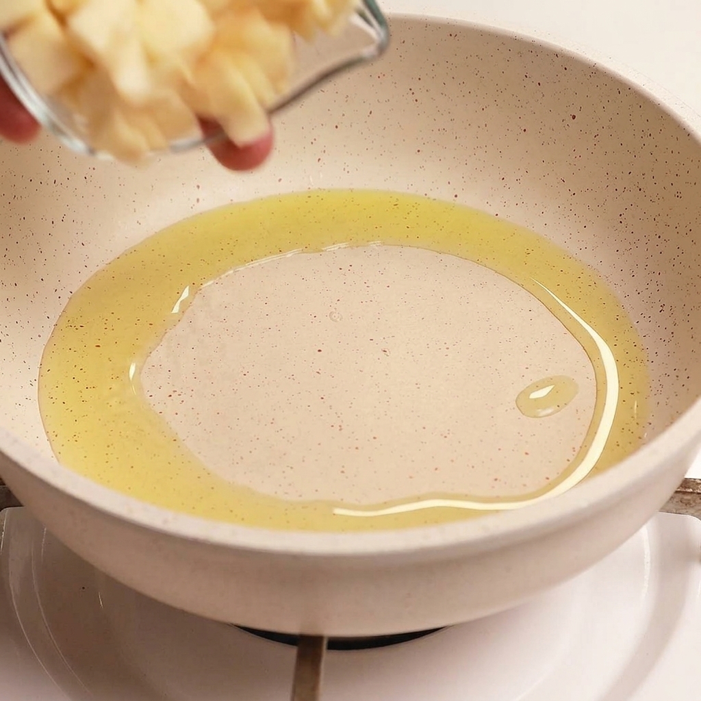Dünne Knoblauchscheiben werden aus einer kleinen Glasschale in eine Pfanne mit heißem, glänzendem Olivenöl gegeben.