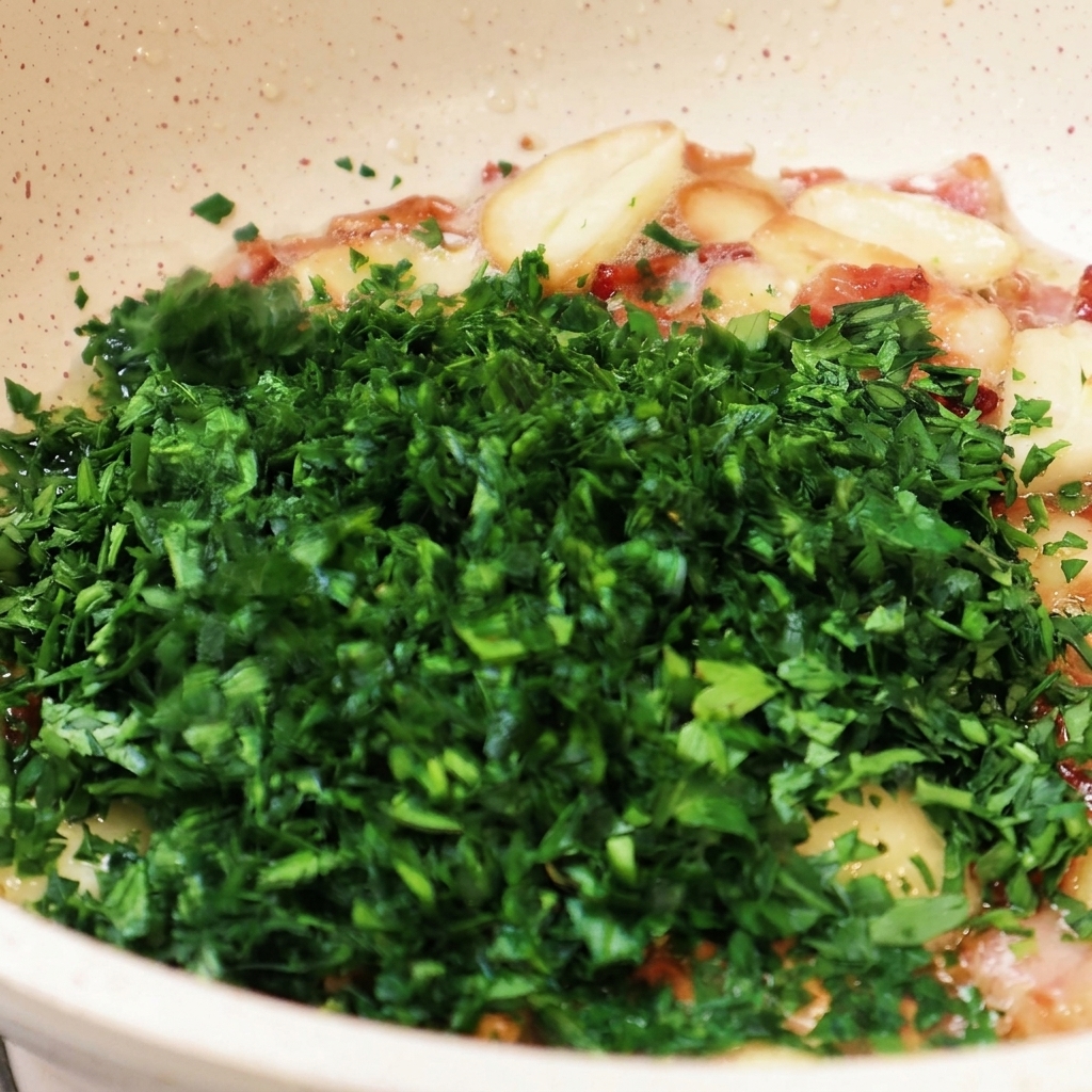 Eine große Menge fein gehackte grüne Petersilie wird in eine Pfanne mit gebratenem Knoblauch und Speckstücken gegeben.