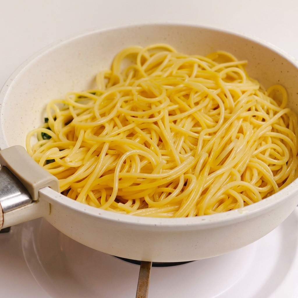 Gekochte Spaghetti liegen auf der Sauce aus grünen Kräutern, Knoblauch und Speck in einer hellen Pfanne.