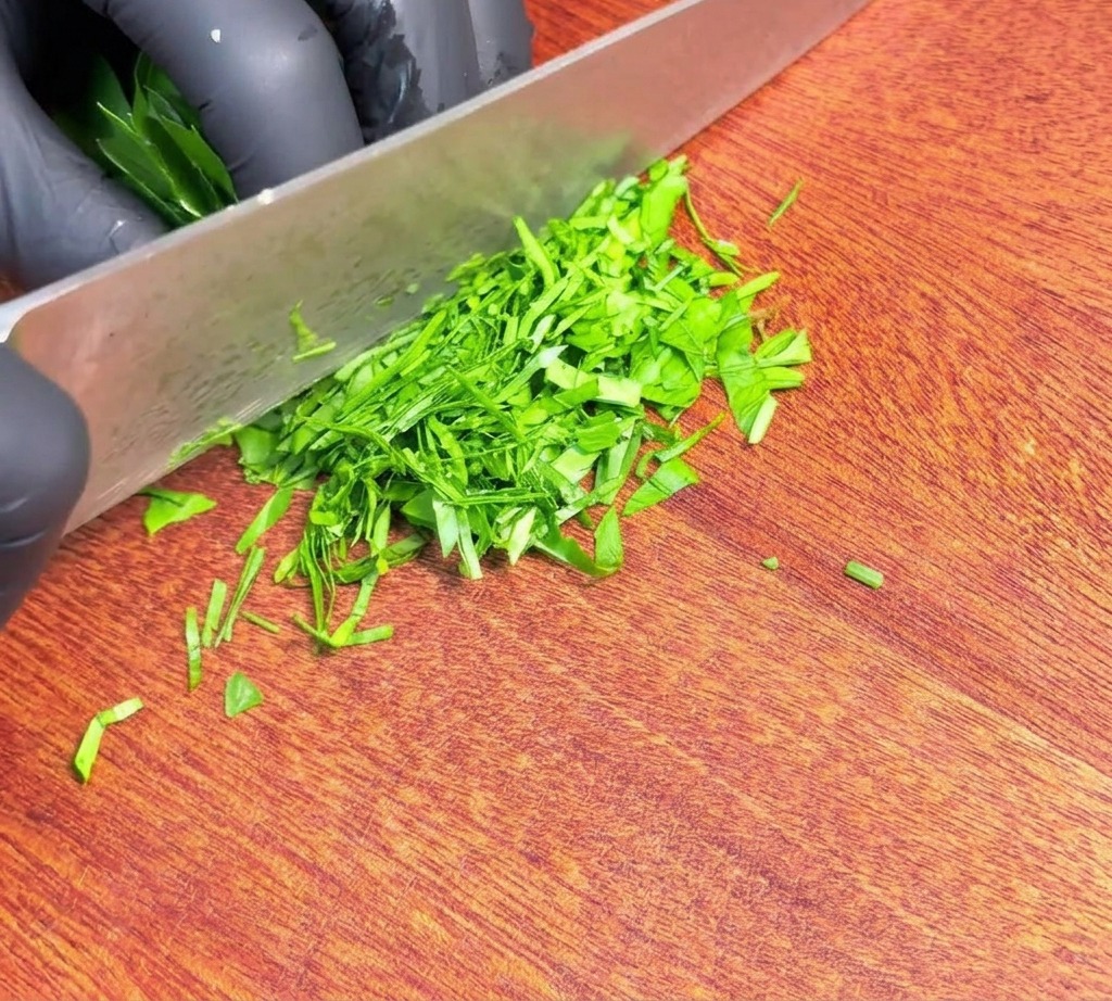 Fein gehackte frische grüne Petersilie liegt neben der Klinge eines scharfen Messers auf einem Holzschneidebrett.