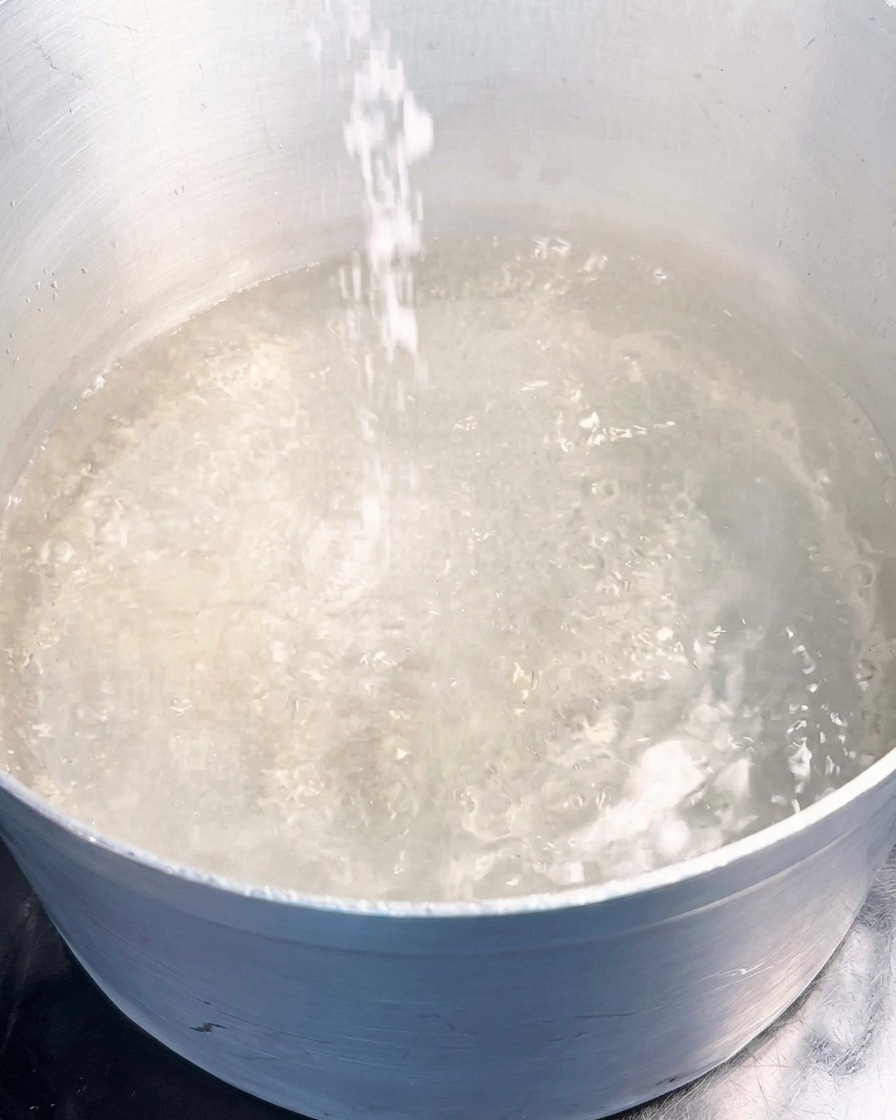 Ein Strahl weißes Meersalz wird in einen Topf mit kräftig sprudelndem, kochendem Wasser geschüttet.