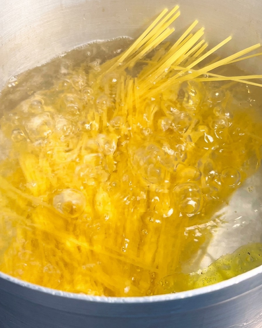 Ein Bündel gelbe, ungekochte Spaghetti wird in einen großen Topf mit sprudelnd kochendem Wasser getaucht.