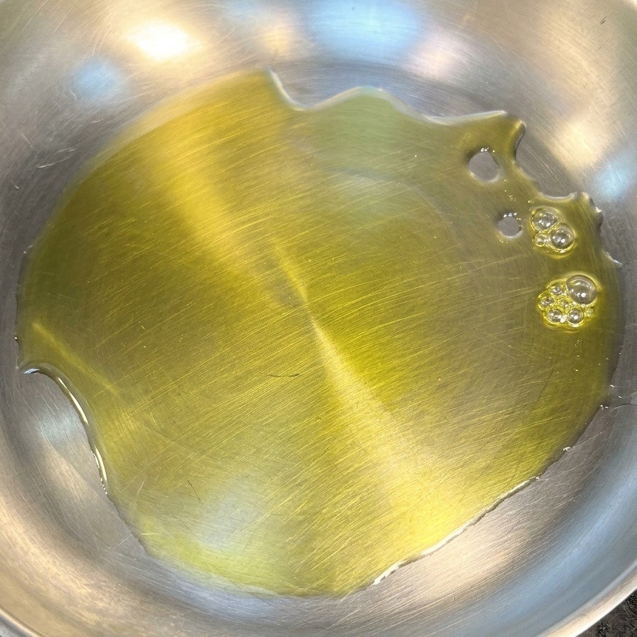 Eine Schicht goldgelbes Olivenöl bedeckt den Boden einer sauberen Edelstahlpfanne.