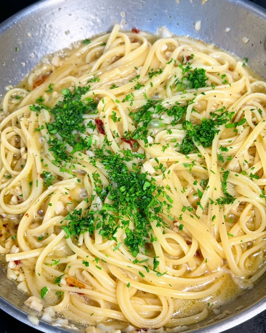 Leuchtend grüne, gehackte Petersilie wird über eine Pfanne mit Knoblauch-Olivenöl-Pasta gestreut.