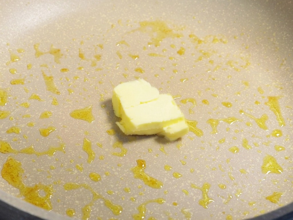 Ein kleines Stück gelbe Butter schmilzt in einer Pfanne mit den Bratrückständen des Olivenöls.