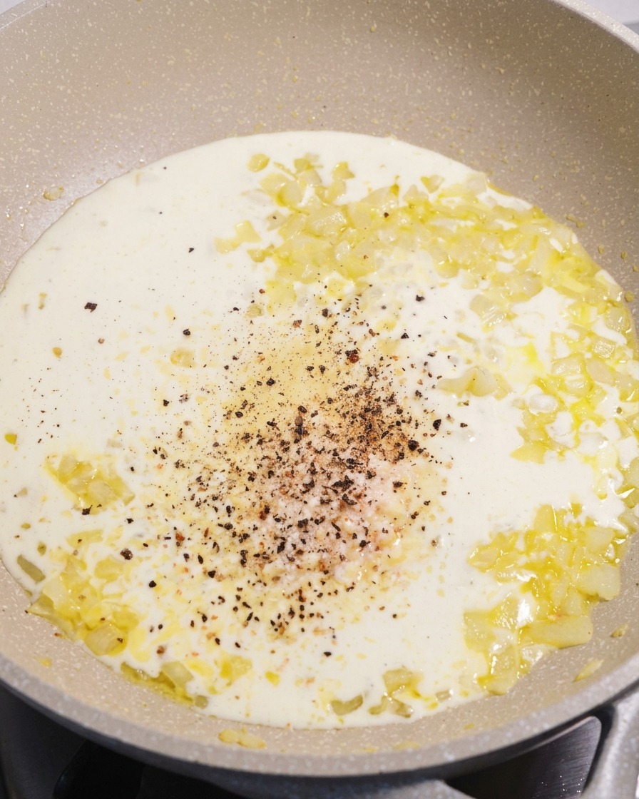Eine Pfanne mit glatter weißer Sahnesauce, in deren Mitte sich frisch gemahlener schwarzer Pfeffer und Parmesan befinden.