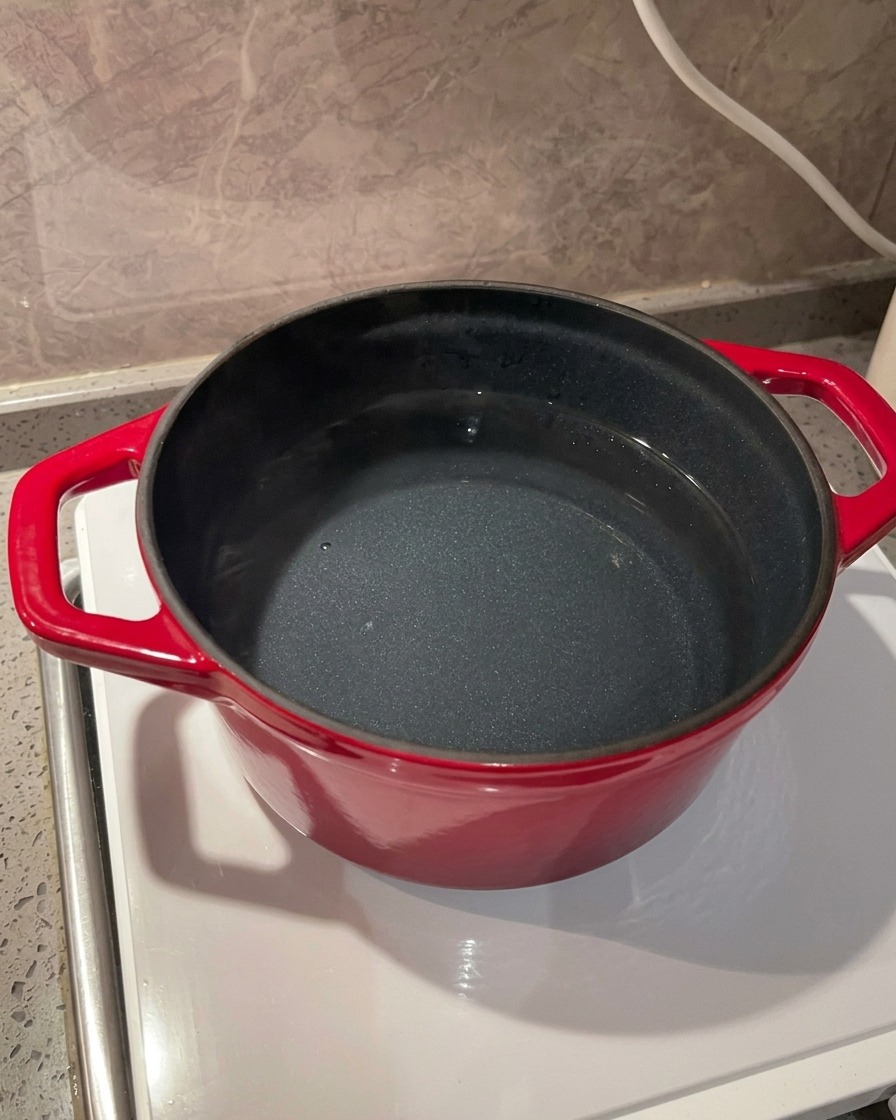 Eine Nahaufnahme von Meersalz, das in einen leuchtend roten Topf mit Wasser auf einem Induktionsherd gestreut wird.