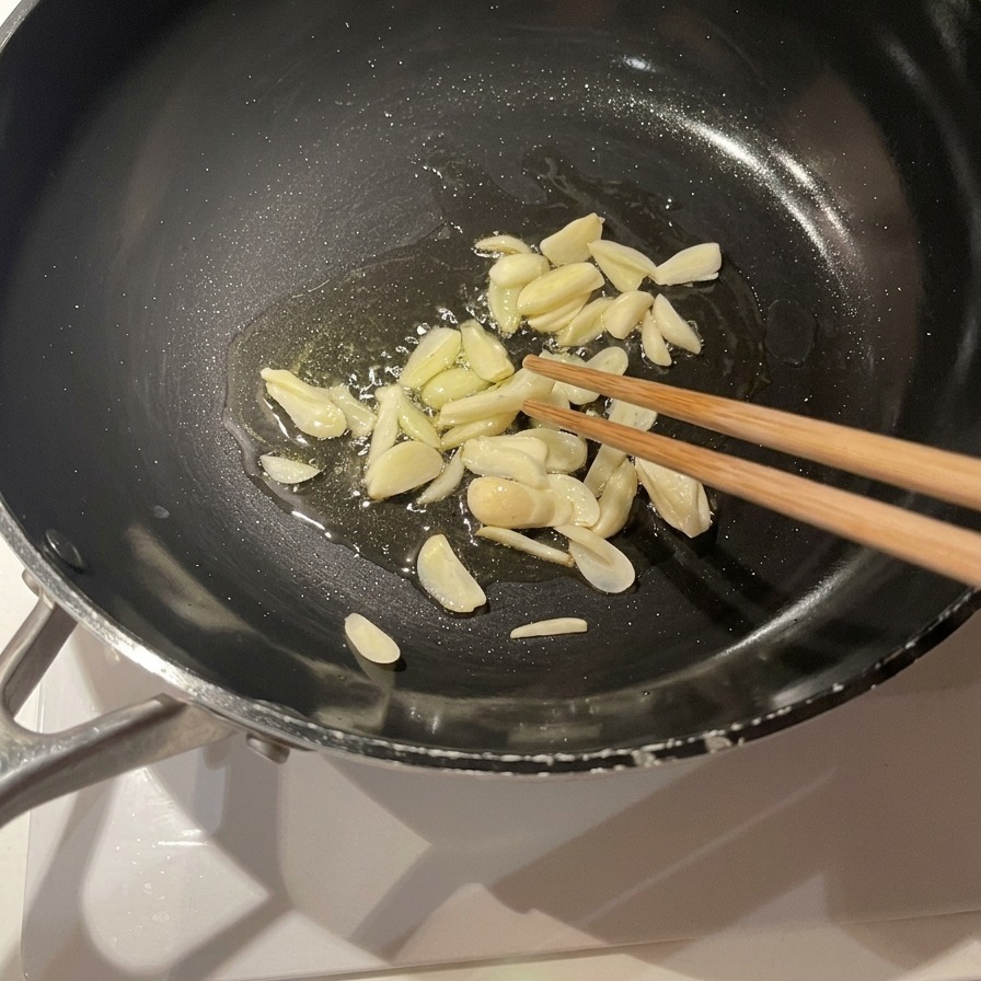 Knoblauchscheiben braten in reichlich Olivenöl in einer schwarzen Pfanne und werden mit Holzstäbchen umgerührt.