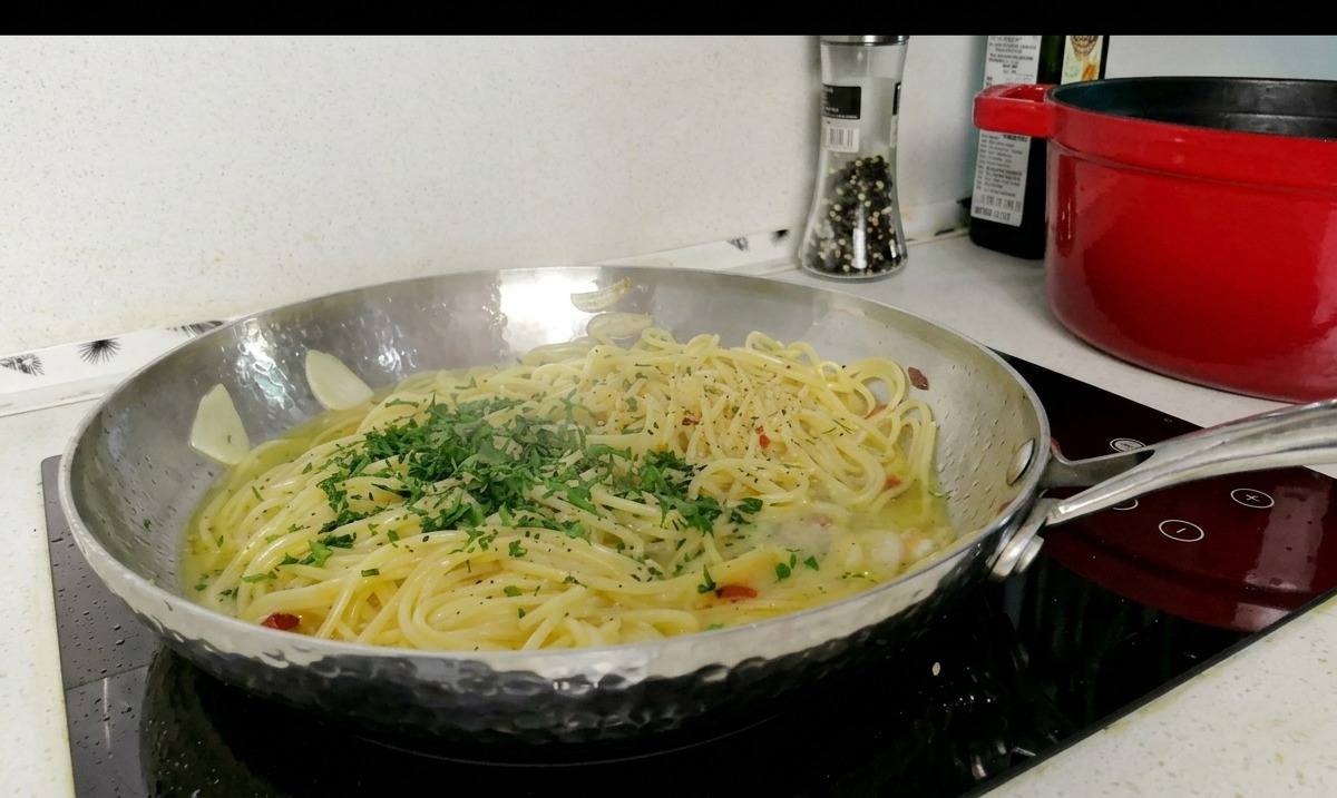 Eine Edelstahlpfanne mit Spaghetti in einer leichten Soße, garniert mit einem Haufen frisch gehackter grüner Petersilie.