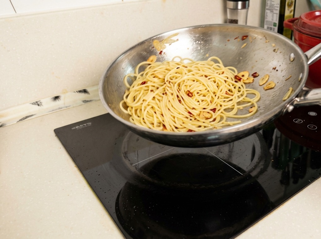 Eine Edelstahlpfanne wird in der Luft geschwenkt, während die Spaghetti von einer glänzenden, emulgierten Soße umhüllt werden.