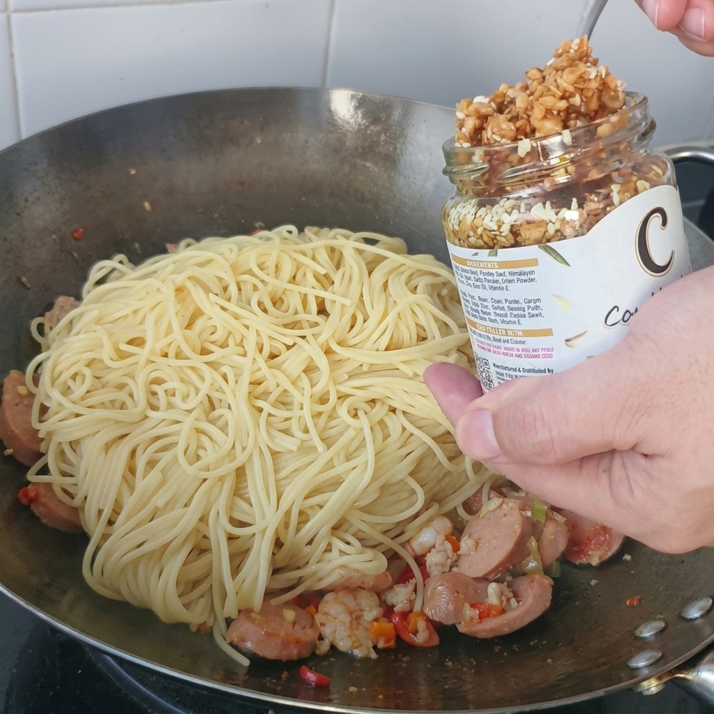 Knuspriger, goldener Knoblauch wird mit einem Löffel aus einem Glas auf einen Berg Spaghetti in einem Metallwok gegeben.