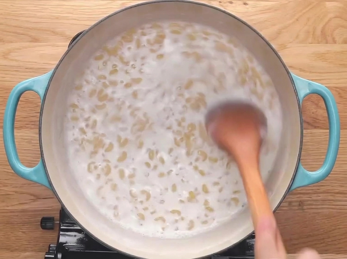 Ein Holzlöffel rührt Hörnchennudeln um, die in Milch köcheln.