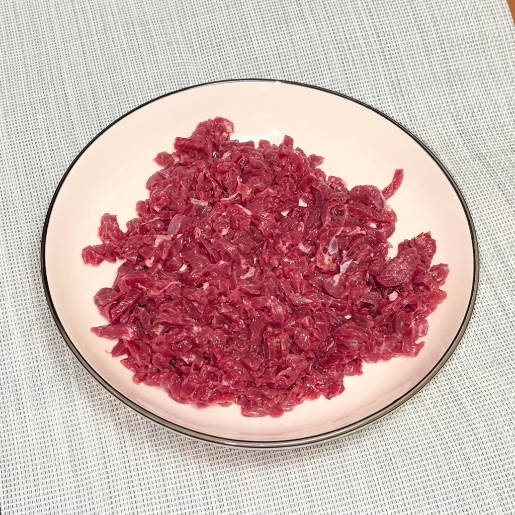 Rohes Rinderhackfleisch in einer weißen Schüssel, bestreut mit schwarzem Pfeffer und Öl zum Marinieren.