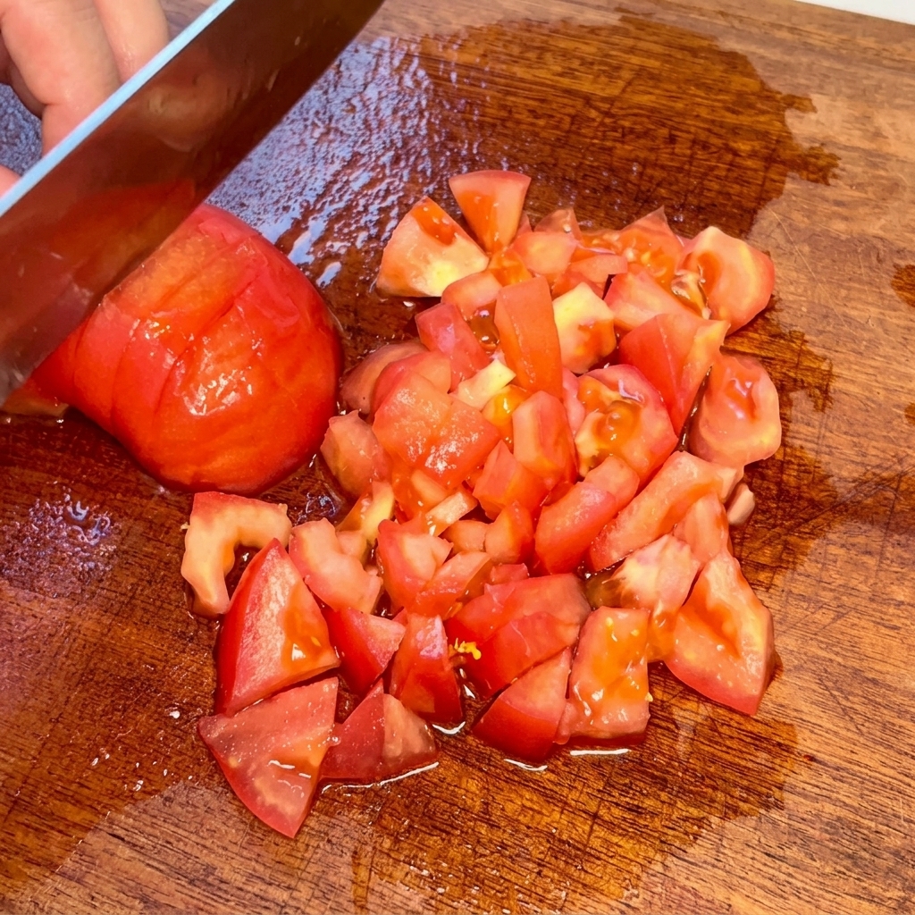 Eine geschälte Tomate wird auf einem Holzbrett in kleine Würfel geschnitten.