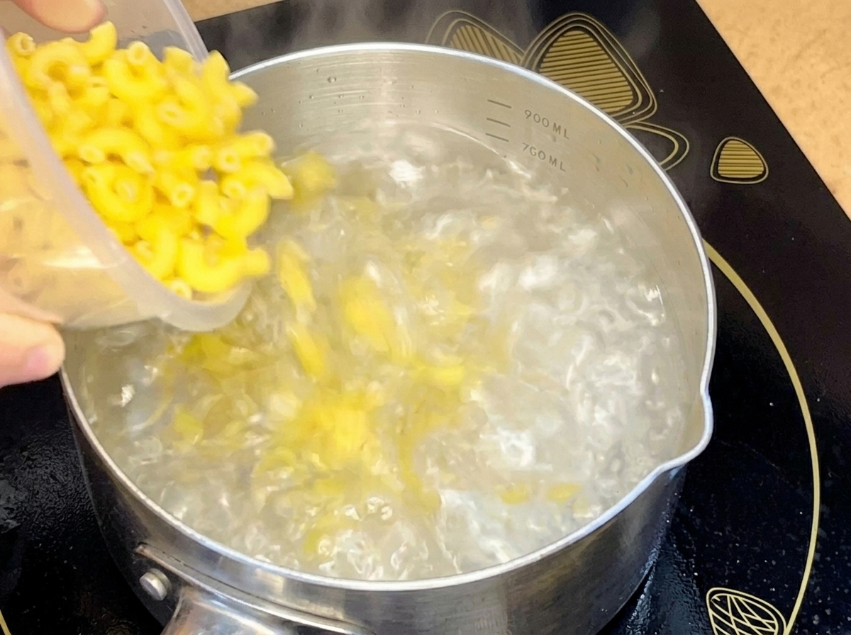 Trockene Makkaroni werden aus einem Behälter in einen Edelstahltopf mit kochendem Wasser geschüttet.
