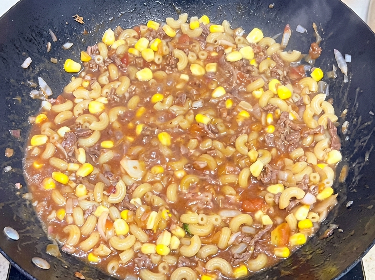 Gekochte Makkaroni werden in einem großen Wok unter eine herzhafte Rindfleisch-Tomaten-Sauce gemischt.