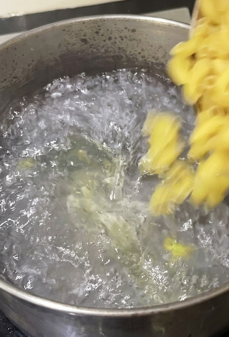 Hörnchennudeln werden aus einer Schüssel in einen Topf mit kochendem Wasser auf dem Herd geschüttet.