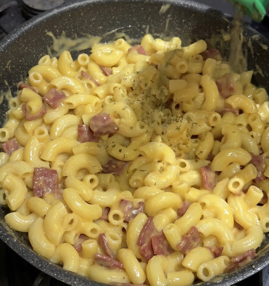 Getrocknete grüne Petersilie wird aus einem grünen Gewürzstreuer auf eine Pfanne voller Mac and Cheese gestreut.