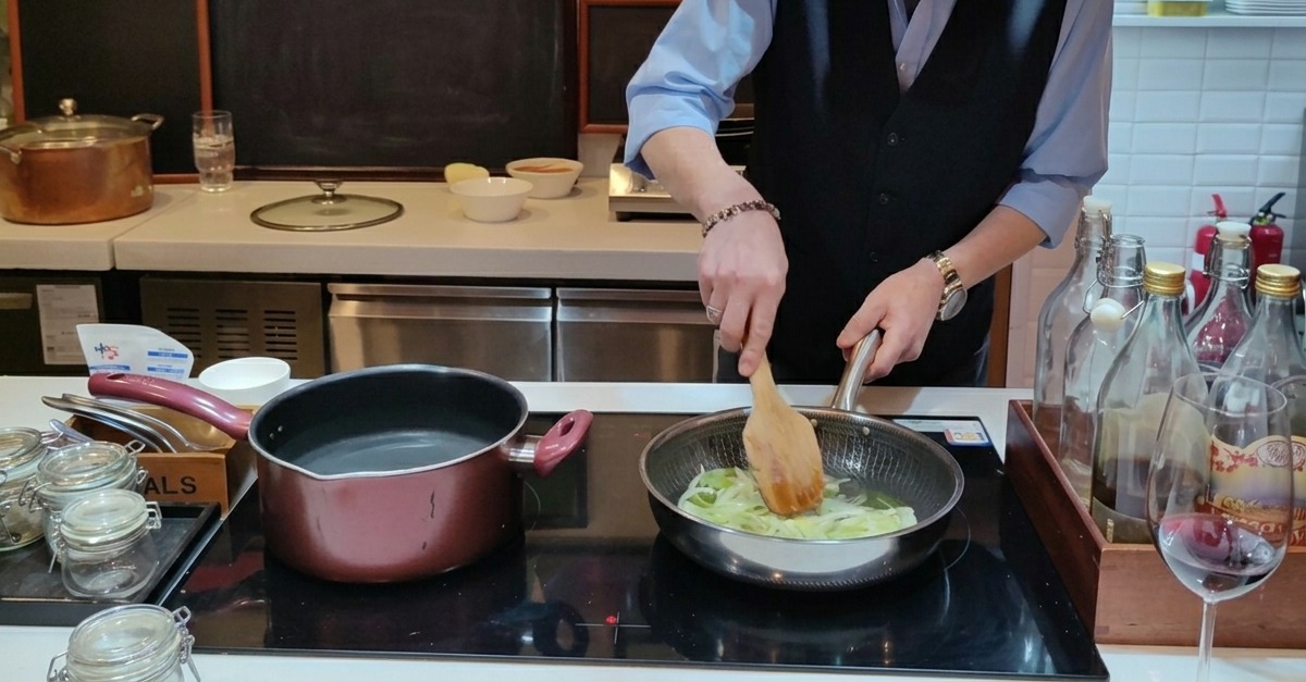 Fein geschnittene Zwiebeln werden mit einem Holzspatel in einer Pfanne mit Olivenöl angedünstet.