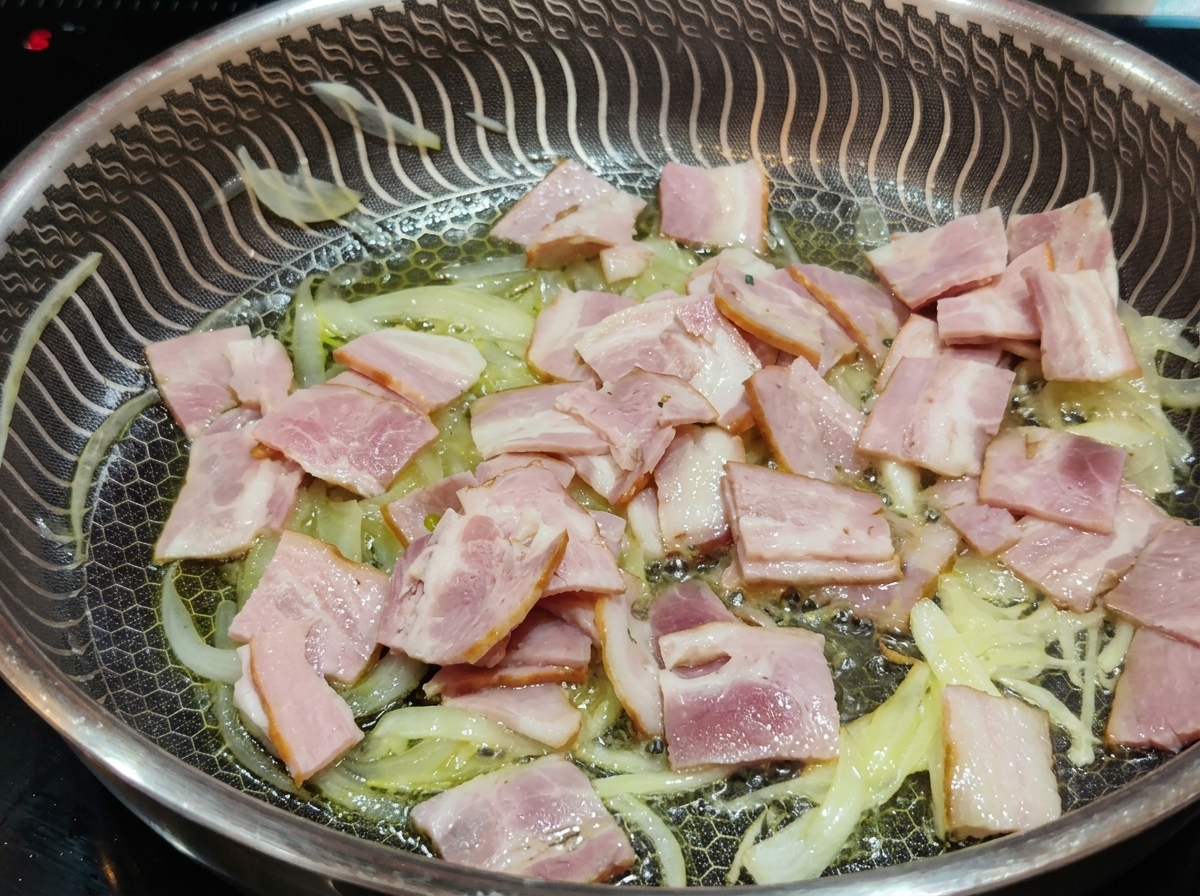 Rosa Speckstreifen braten zusammen mit weichen, glasigen Zwiebeln in einer Pfanne mit Öl.