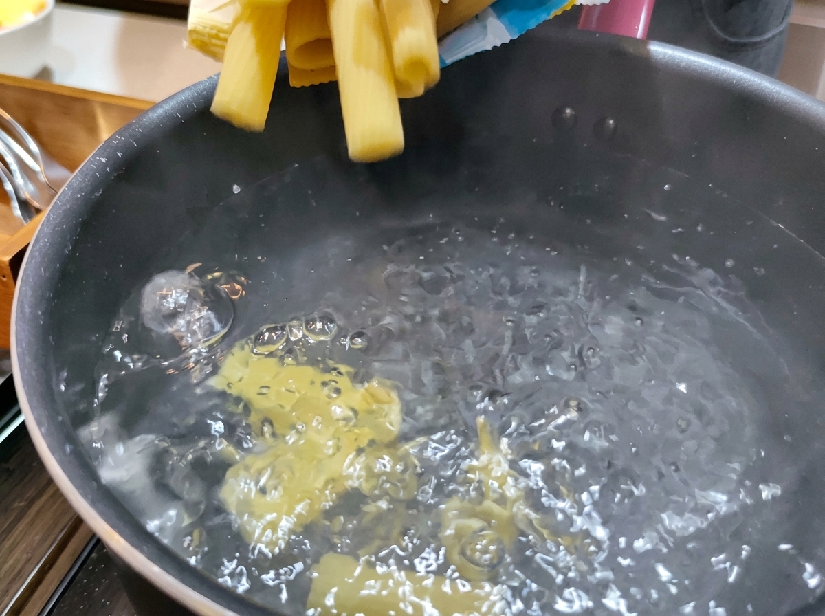 Trockene, gelbe Rigatoni-Nudeln werden in einen Topf mit sprudelnd kochendem Wasser gegeben.