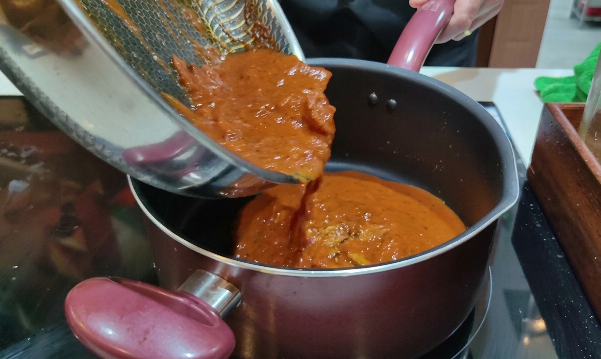 Die fertige, rote Amatriciana-Sauce wird aus der Pfanne direkt in den Topf mit den abgegossenen Rigatoni gegossen.